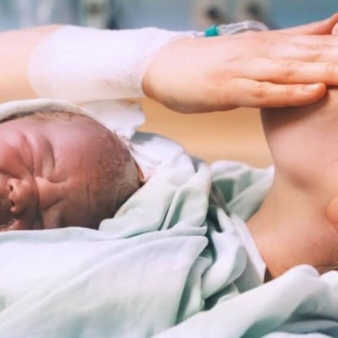 A mother holds her newborn baby and wipes a tear after a VBAC delivery.