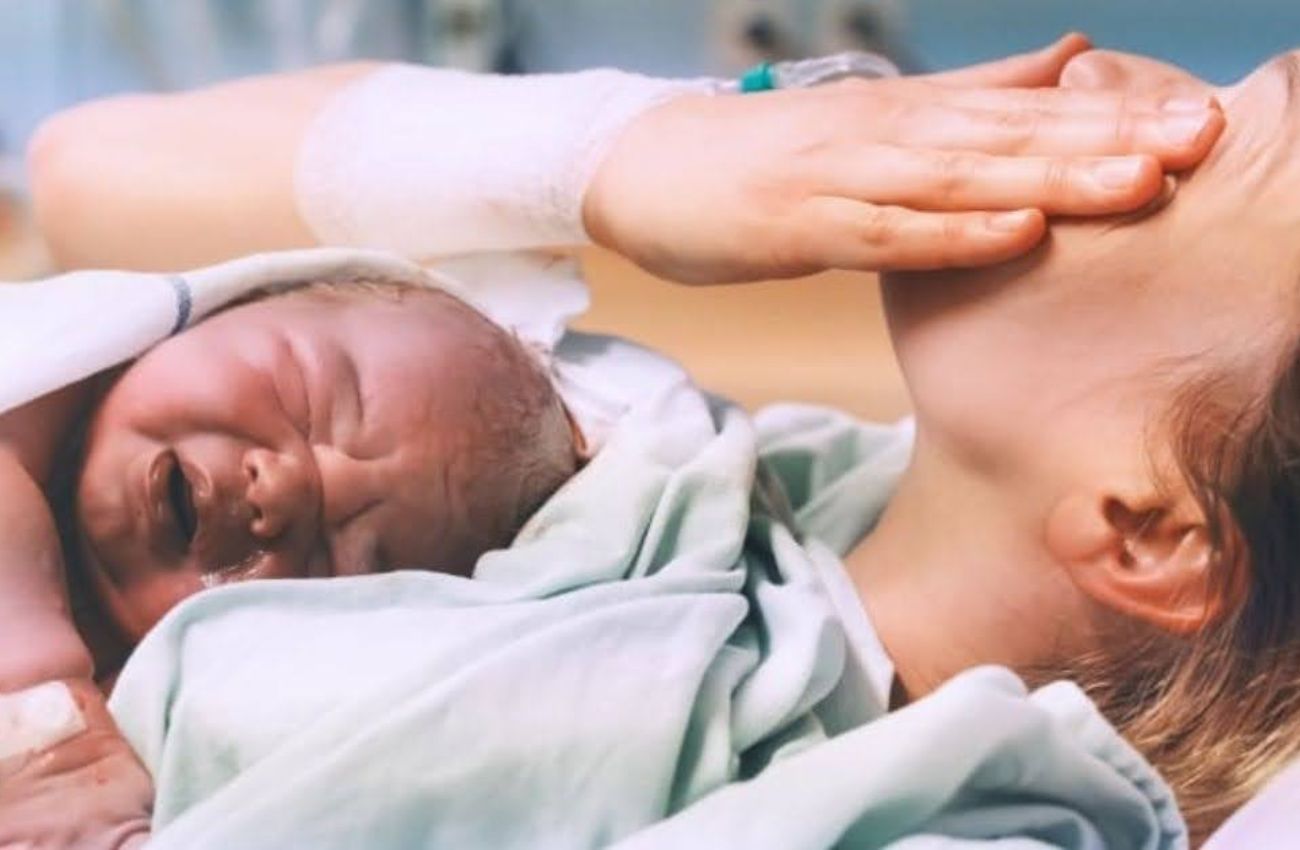 A mother holds her newborn baby and wipes a tear after a VBAC delivery.