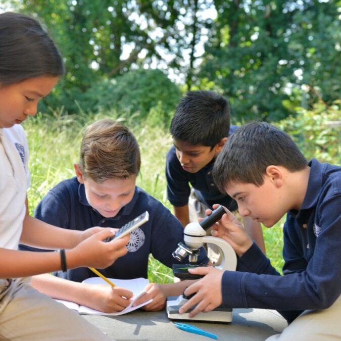 Students work on a lesson with a microscope outdoors at Main Line Classical Academy.