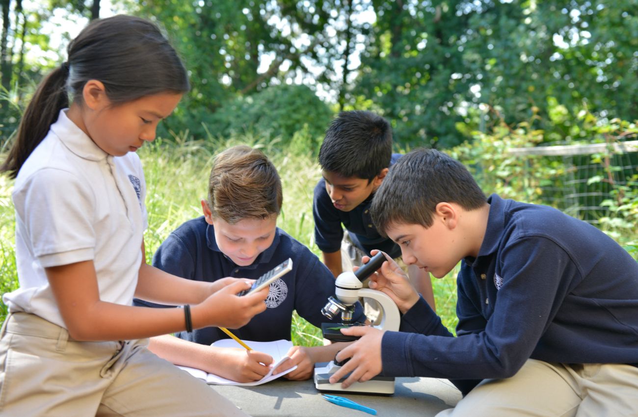 Students work on a lesson with a microscope outdoors at Main Line Classical Academy.