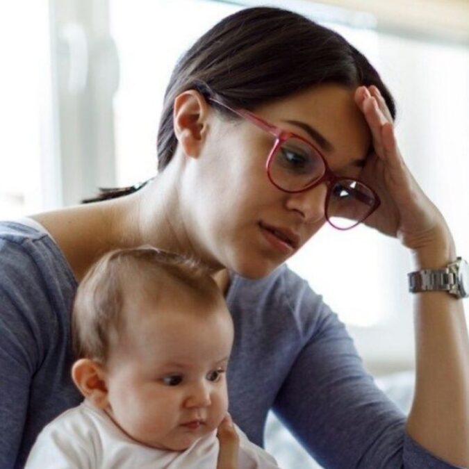 A mom holds her baby, while grappling with the mental load of motherhood.