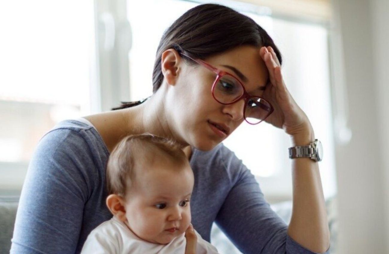 A mom holds her baby, while grappling with the mental load of motherhood.
