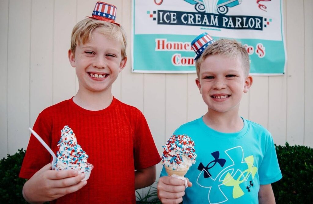 Two boys with tiny patriotic top hats hold ice cream with red and blue sprinkles. 