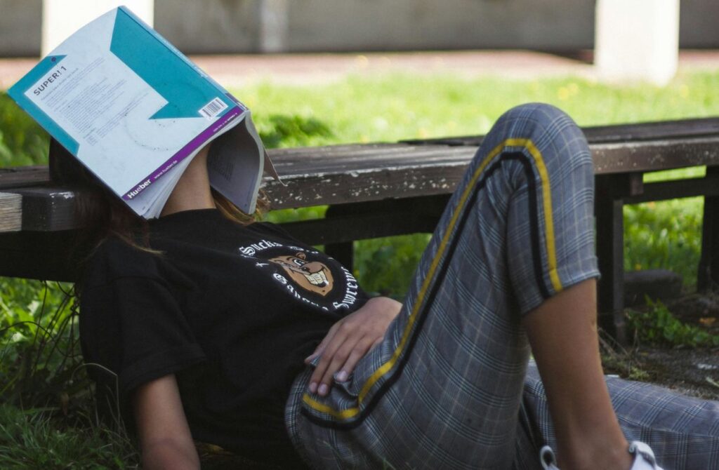 A young adult snoozes with her workbook over her face.