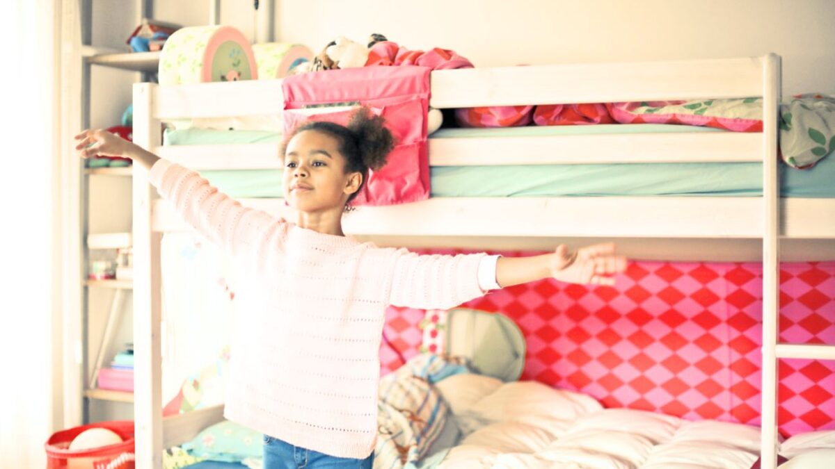 A young girl stands poses in her bedroom with a calm demeanor.