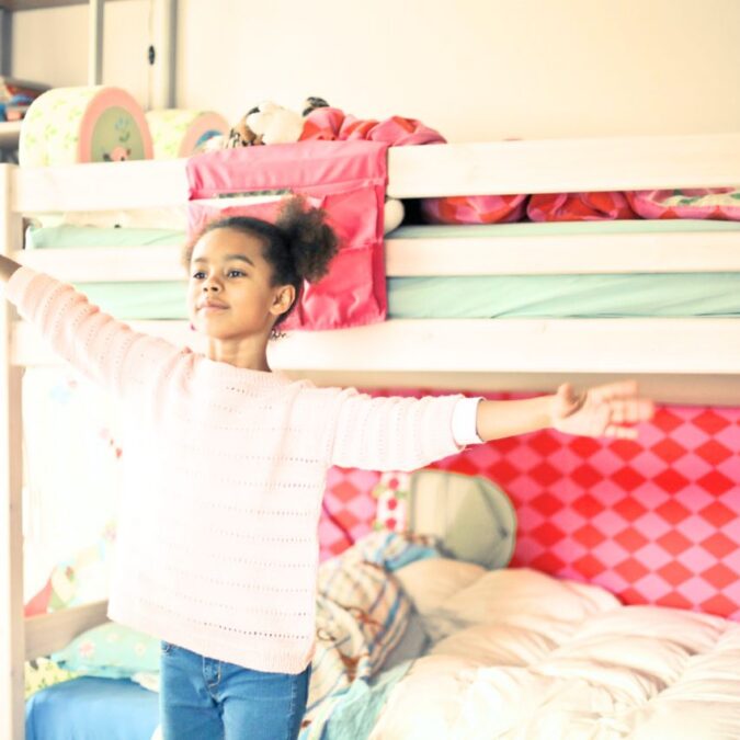 A young girl stands poses in her bedroom with a calm demeanor.