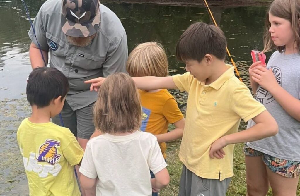 Kids gather around a Hiking Hounds Adventures leader to learn about fishing, a great kids fall activity.