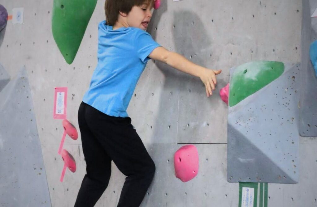 A boy in a blue t-shirt reaches for a hold on an indoor climbing wall at Reach Climbing and Fitness in Bridgeport, PA.