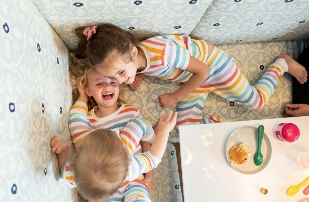 Three children in striped pjs laugh in the breakfast nook by documentary family photographer Polina Bulman.