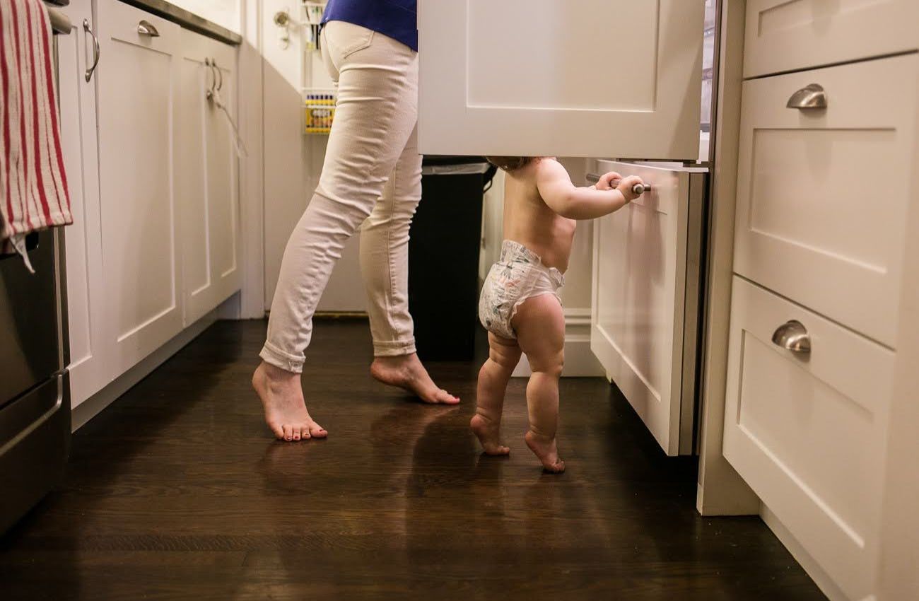 A mother and baby stand on tippy toes in the kitchen by documentary family photographer Polina Bulman.