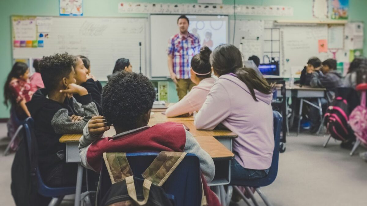 A teacher stands in front of a classroom of teen students.