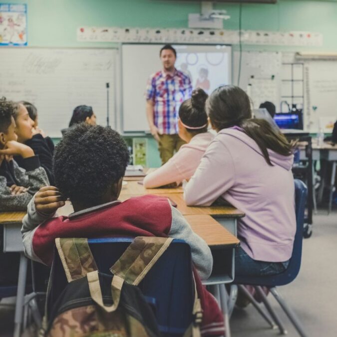 A teacher stands in front of a classroom of teen students.