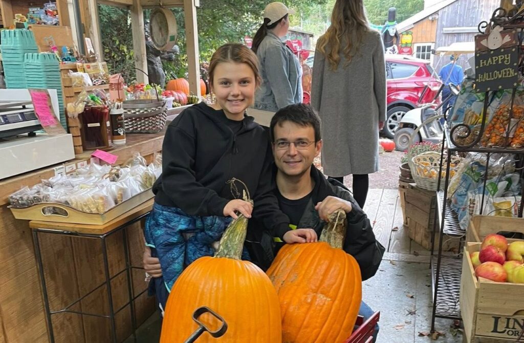 Father and daughter pose with pumpkins in a wagon and Indian Orchards Farm.